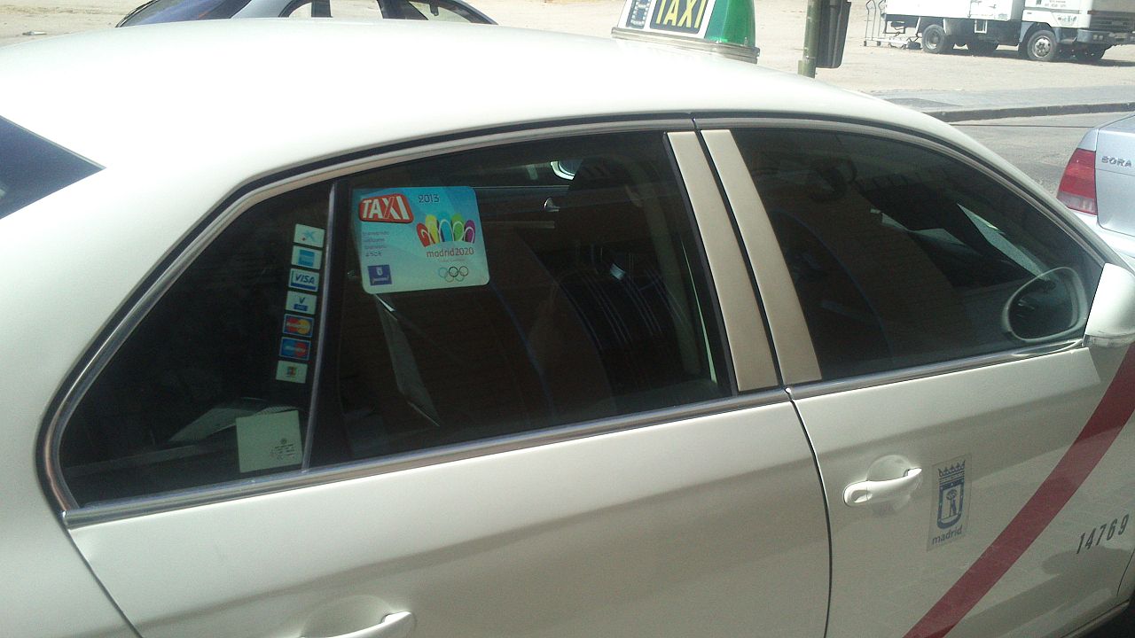 Puerta de un taxi blanco de Madrid, con el escudo de la ciudad y el cartel de taxi.