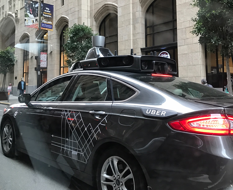 Coche gris de pruebas con un bloque de sensores en el techo y la palabra Uber en la puerta.
